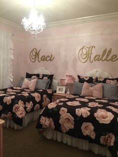 two beds in a room with pink and black bedding, chandelier and name on the wall