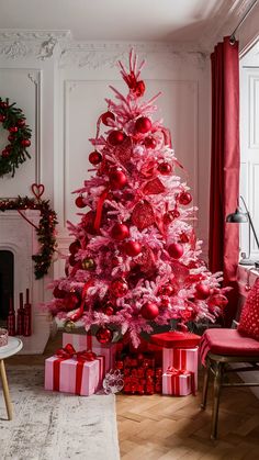 a pink christmas tree in a living room decorated with red and silver ornaments, presents and decorations