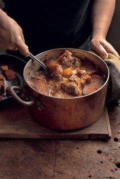 a person cooking food in a pot on top of a wooden cutting board with a spoon