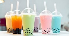 four different colored drinks are lined up on the table with straws in each cup