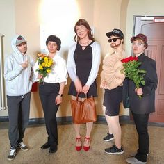 four people standing in front of a wall holding flowers