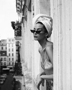 a woman wearing sunglasses and a towel on her head leaning against a wall in the city