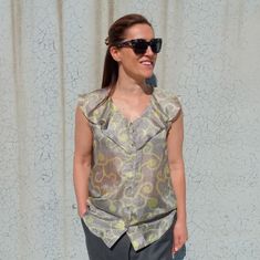 a woman standing in front of a curtain wearing sunglasses and a top with flowers on it