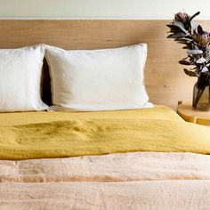 a bed with two white pillows and a yellow blanket on top of it next to a plant