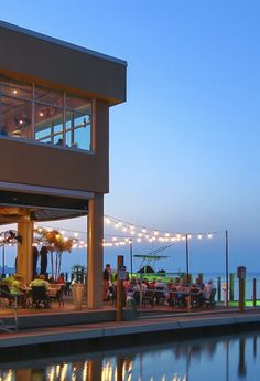 an outdoor dining area overlooking the water at dusk with string lights strung across the patio