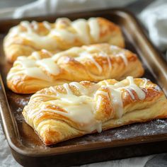 two croissants with white icing sitting on a baking tray next to each other