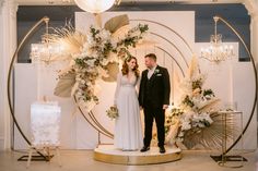 a bride and groom standing in front of a wedding arch decorated with flowers, greenery and chandeliers