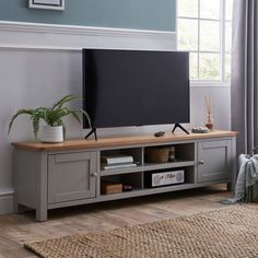 a flat screen tv sitting on top of a wooden entertainment center next to a window