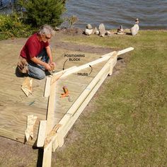 a man working on a wooden deck next to the water with ducks in the background