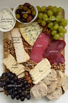 an assortment of cheeses, meats and grapes on a board