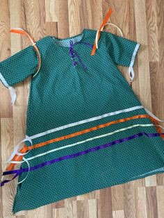 a child's green dress with orange, white and blue strips on the bottom