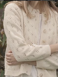 a woman standing with her arms crossed wearing a white sweater and cardigan, looking at the camera