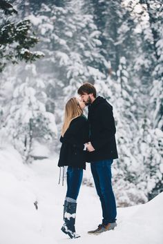 a man and woman standing in the snow with their arms around each other as they kiss