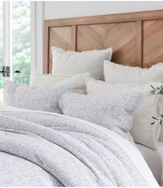 a bed with white and grey linens is shown in front of a wooden headboard