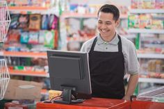 a man standing in front of a computer on top of a red counter at a grocery store