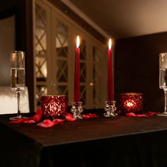 candles are lit on a table with red rose petals