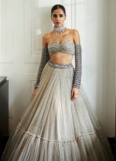 Embrace the elegance with this Grey Crystal and Sequin Embroidered Tulle Lehenga Set, a masterpiece of sophistication. Crafted from soft net and georgette, the grey lehenga features intricate hand-embroidered sequins and crystal embellishments, creating a captivating shimmer with every movement. Paired with the jewelled blouse showcases a strapless neckline, adorned with crystal embellishments, adding a glamorous touch to the look. Completed with a matching dupatta and statement arm cuffs enhance the outfit with a modern, regal twist. Perfect statement lehenga for weddings, receptions, or cocktail. Composition : Lehenga, Dupatta - Soft Net and Blouse - Soft Net and Georgette Care: Dry Clean Only and Vacuum Storage This product can be customized for sleeves, blouse length and neckline Deliv Tulle Lehenga, Grey Lehenga, Lehenga Dupatta, Weddings Receptions, Crystal Embroidery, Arm Cuffs, Vacuum Storage, Indian Wedding Wear, Strapless Neckline