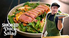 a man holding a plate with meat and vegetables on it next to a bowl of salad