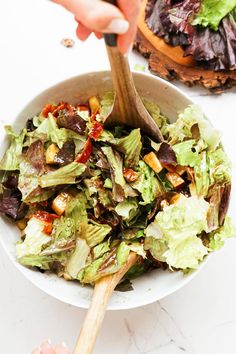 a person holding a wooden spoon in a bowl filled with lettuce and other vegetables