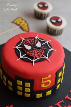 a spiderman themed birthday cake with cupcakes in the background