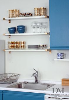 a kitchen with blue cabinets and shelves filled with glasses, cups and bowls on top of them