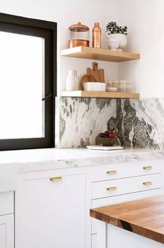 a kitchen with marble counter tops and open shelves on the wall next to an open window