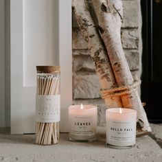 two candles sitting next to each other in front of a fireplace