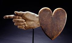 a wooden heart shaped object with two hands holding it up to the other hand, on a black background