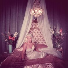 a woman in a white dress sitting on a bed with a canopy over her head