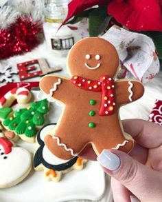 a person holding up a decorated gingerbread in front of other cookies and christmas decorations