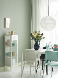 a dining room with green walls and white table, chairs and vase on the floor