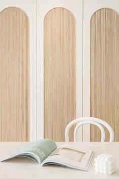 an open book sitting on top of a table next to a white chair and wooden doors