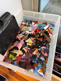 a plastic container filled with lots of different colored paper pieces next to a black box