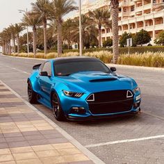 a blue sports car is parked on the side of the road in front of palm trees