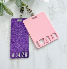 two pink and purple luggage tags sitting on top of a white table next to a plant