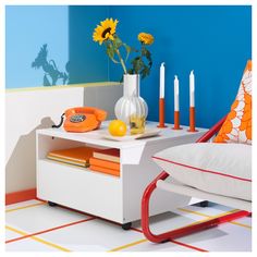 a white table topped with a vase filled with yellow flowers and orange candles next to a chair