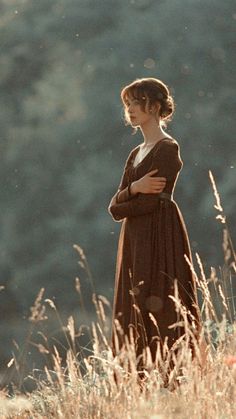 a woman standing in tall grass with her arms folded and looking off into the distance