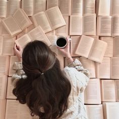 a woman laying on top of a pile of books next to a cup of coffee