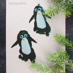 two paper penguins are sitting on top of a piece of paper next to pine branches