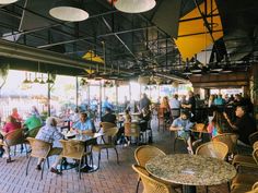 many people are sitting at tables and chairs in an outdoor dining area with umbrellas