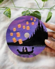 a person holding up a purple cd with orange squares on it and a black cat