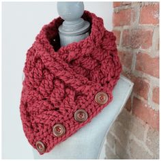 a red knitted cowl with buttons on the front and side, sitting next to a brick wall