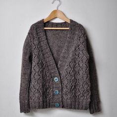 a gray cardigan sweater hanging on a wooden hanger with a white wall in the background