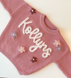 "custom hand embroidered sweaters for babies and toddlers. the perfect keepsake gift for a baby shower, birthday, holiday, milestone photos, etc. 🤍  turn around time: 1-2 weeks *please choose size/color and number of letters from the drop down. prices increase with name length due to the time required to embroider *flower over \"i\" as dot or 1-2 flowers next to name is free of charge! only choose +design for all over design *longer names on smaller sweaters typically need a thinner yarn - max number of characters is 6 using chunky yarn, then I will use a thinner yarn for anything longer. but message me if you have a long name on a small sweater so I can verify it will fit   PERSONALIZATION 1.) Name or word (CASE SENSITIVE) 2.) Yarn color for name  3.) design & yarn color (flowers, suns, Embroider Flower, Embroidered Sweaters, K Names, Name Sweater, Milestone Photos, 2 Flowers, All Over Design, Star Embroidery, Small Sweater