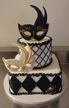 a three tiered cake decorated with black and white icing, topped with a masquerade mask