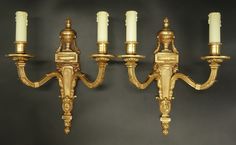 three golden wall lights with white candles on each one and black back ground behind them