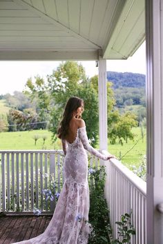 a woman standing on a porch next to a flower bush wearing a long sleeved dress