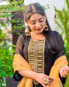 a woman in a black and yellow outfit looking down at something on her hand while standing next to some plants