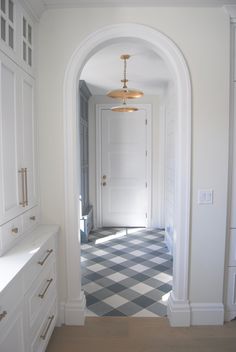 an archway leads into a hallway with checkered tile flooring and white cabinetry