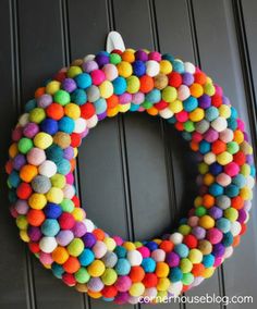 a colorful wreath with pom - poms hanging on the front door to decorate it